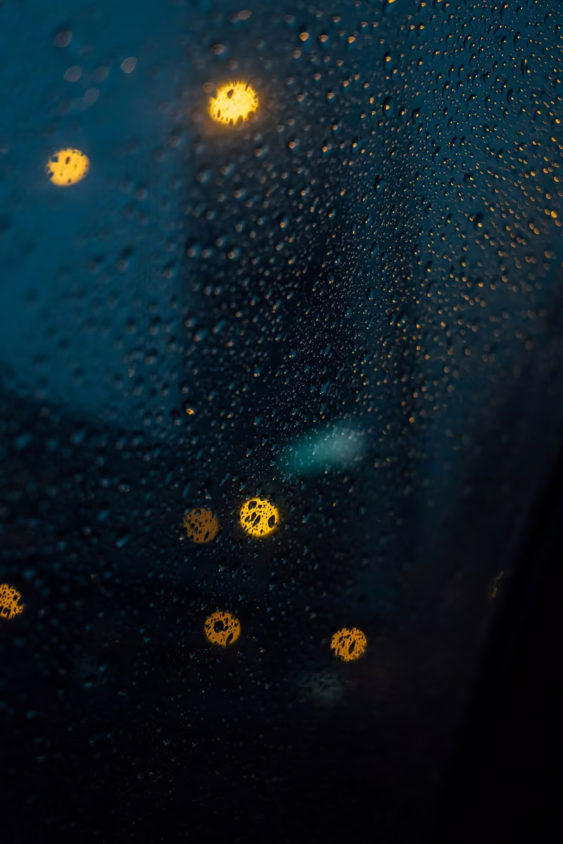 Gotas de chuva numa janela, com luzes desfocadas ao fundo