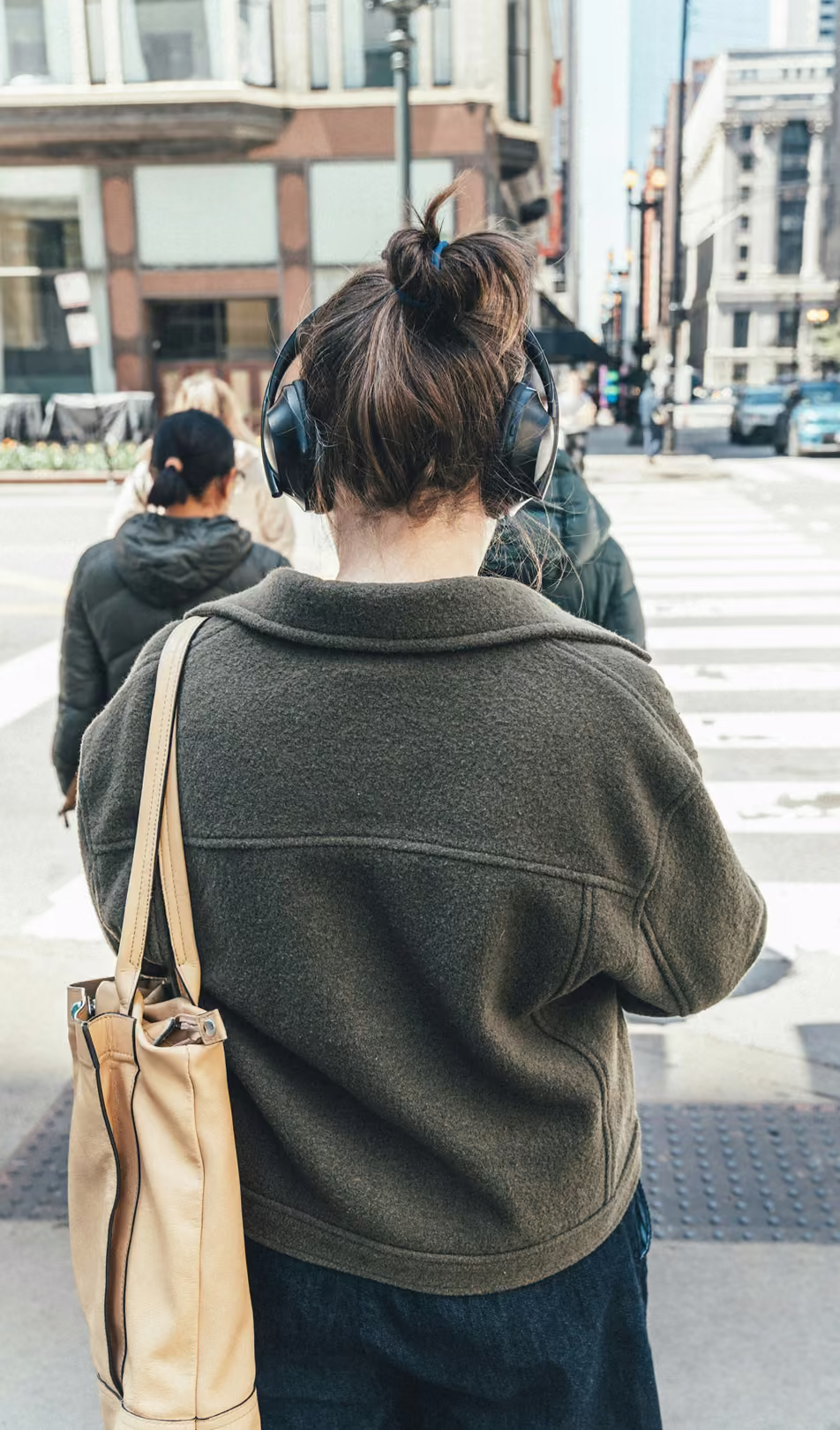 Pessoa de costas, com fones de ouvido, esperando para atravessar a rua