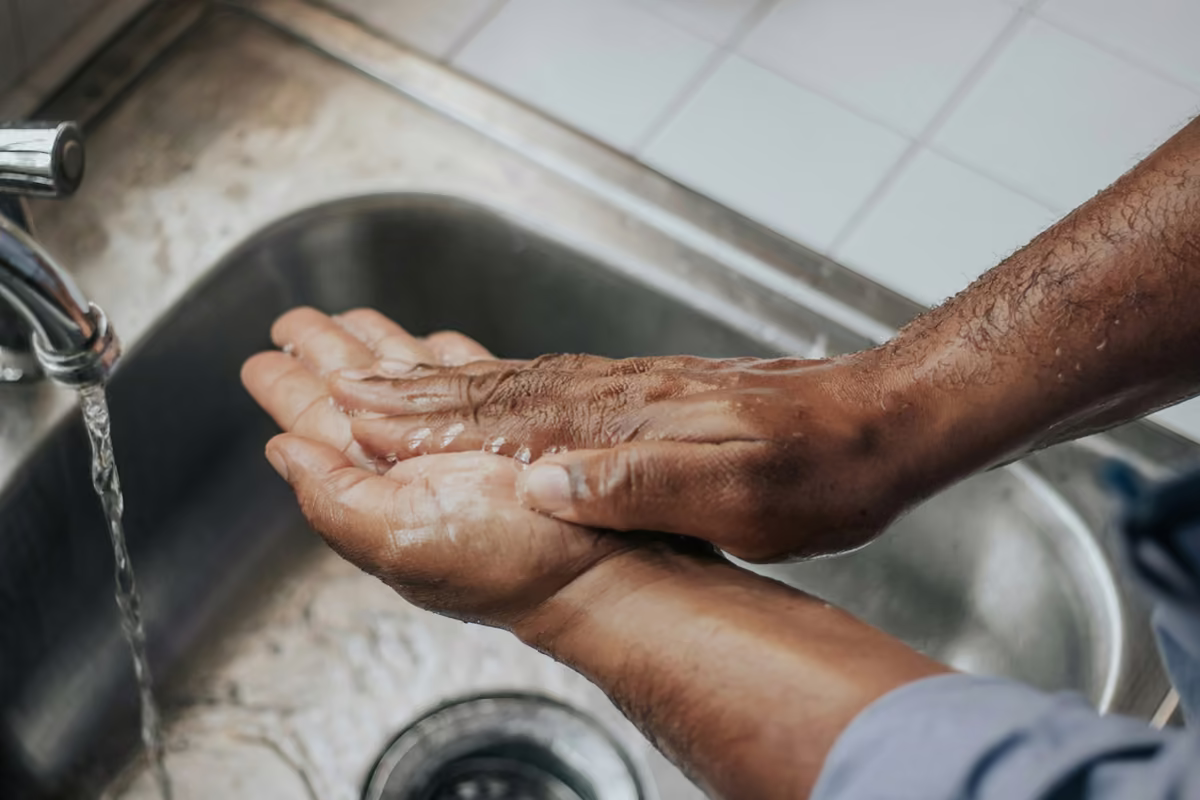 Mãos sendo lavadas com sabão numa pia de inox